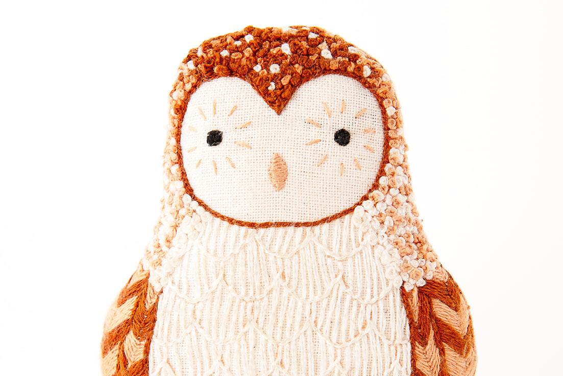 Embroidered owl stuufed toy with a white face and brown body on a white background