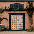 Quilt with floral pattern displayed on a wooden frame against a pink wall with greenery.