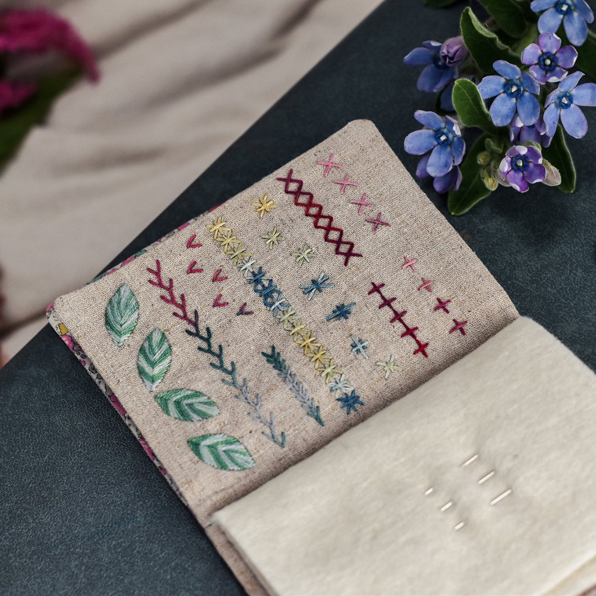 Embroidered fabric with stitch samples on a dark surface with flowers in the background