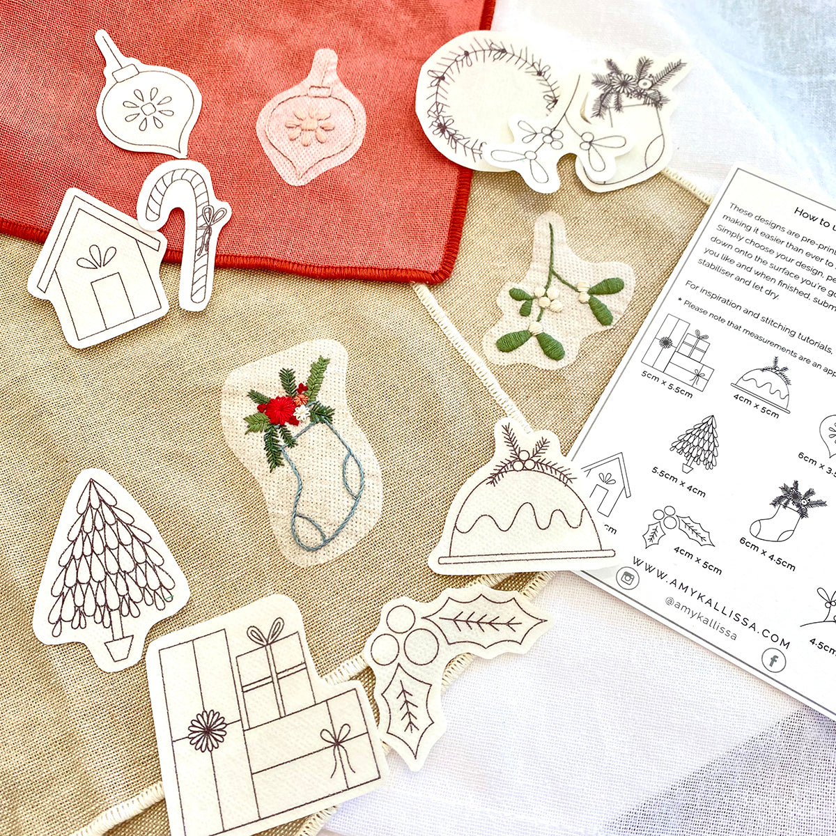 Set of Christmas-themed embroidered patterns on a fabric surface with a printed sheet of instructions.
