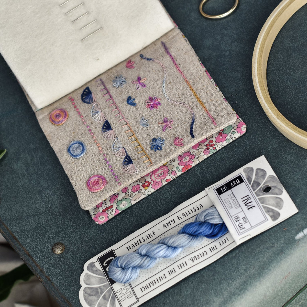 Embroidery work with floral patterns on fabric, accompanied by yarn and a needle on a dark surface.