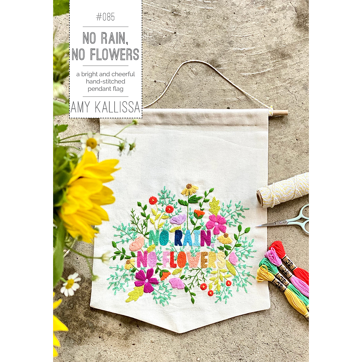 Embroidered banner with colorful floral design and text on a wooden surface.
