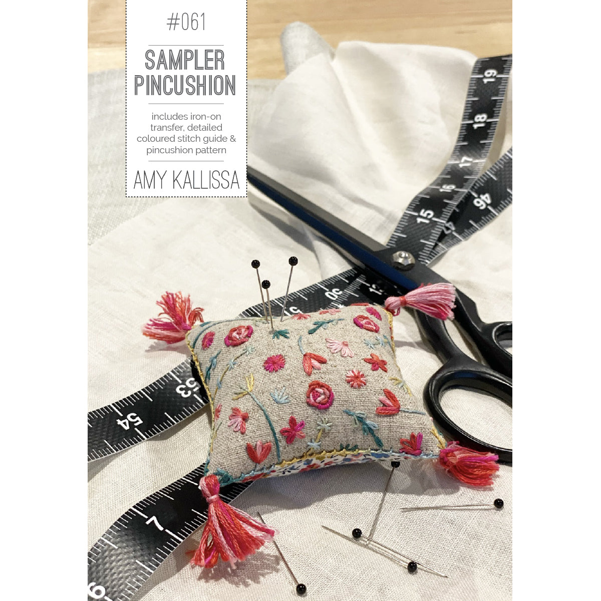 Embroidered pincushion with floral design on a wooden surface with scissors and pins.