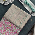 Embroidered fabric with floral pattern and stitch samples, surrounded by embroidery supplies on a dark surface.